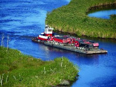 Initially, the client's tug and barge looked like the best way to transport hot mix to the island paving site. On closer examination, however, it was decided to rent a second barge to more efficiently carry twice as many trucks to the site at one time.