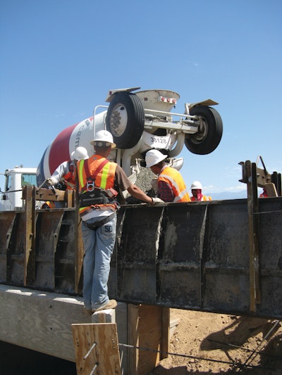 A four-man crew works quickly to pour and finish a typical parapet. One worker uses a power vibrator to consolidate the concrete for uniform density and blend the concrete together into a single solid mass.