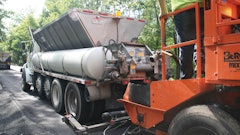 A paving crew member connects the Mobile Support Unit’s asphalt emulsion tank and water tank to the slurry paver and opens the gate to the aggregate hopper, allowing the paver to continually place the surface treatment.