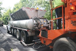 A paving crew member connects the Mobile Support Unit’s asphalt emulsion tank and water tank to the slurry paver and opens the gate to the aggregate hopper, allowing the paver to continually place the surface treatment.