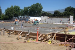 Construction workers pour concrete for the main stage; seating area in the background.