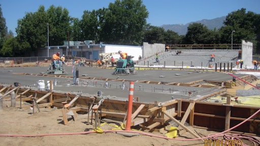 Construction workers pour concrete for the main stage; seating area in the background.