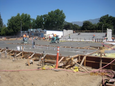 Construction workers pour concrete for the main stage; seating area in the background.
