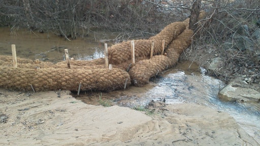 Erosion control products, including coir logs and jute mesh matting, slow erosion in the existing stream. Silt that used to end up in Lake Norman is visible in the foreground of the photo.