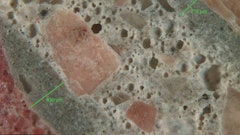 Figure 1: Reflected light photomicrograph of polished surface showing dark, low w/cm mortars (green bars) coating aggregate particles. These are typical indicators of retempering.