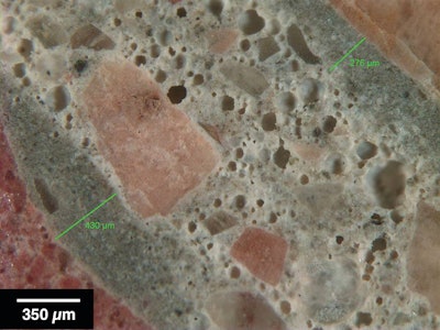 Figure 1: Reflected light photomicrograph of polished surface showing dark, low w/cm mortars (green bars) coating aggregate particles. These are typical indicators of retempering.