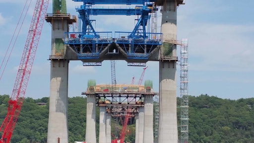 The new St. Croix River Bridge will span between Minnesota and Wisconsin near Stillwater, Minn. Shown here are the piers, cross beams, first precast segments in place, and the extra-dosed towers. The blue structure is a “segment lifter” that lifts castings into position from barges weighing as much as 180 tons.