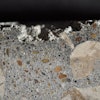 Photograph of polished surface from a concrete core removed from a poorly cured slab on ground showing layer of dark paste at the top of the core. Scale in millimeters. The loss of material at the top is due to poor hydration.
