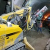 Workers use a Brokk 400D with a TEI 350 rock drill to drill through a tunnel wall. Crews used the attachment to drill holes for steel spiles, well points and freeze pipes.
