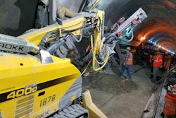 Workers use a Brokk 400D with a TEI 350 rock drill to drill through a tunnel wall. Crews used the attachment to drill holes for steel spiles, well points and freeze pipes.