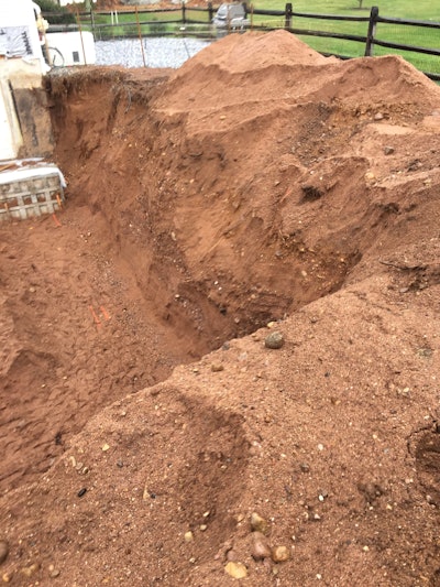 Figure 1: Residential basement excavation with over 8-ft of depth. No benching, loose soil encumbrances on the slope and spoil piles closer than 2-ft from the opening. This excavation should not be entered until corrected.