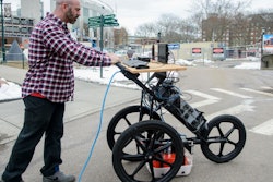 UVM post-doctoral student Dylan Burns demonstrates how the cognitive ground penetrating radar apparatus could be wheeled over an area to scan and map underground infrastructure. The GPR unit, housed in the box near the ground, can peer six to 12 feet down.