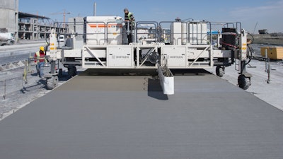 The integrated spraying system of the Wirtgen TCM 95 texture curing machine is spreading a dispersion on the concrete surface. It prevents premature drying of the concrete surface and edges.