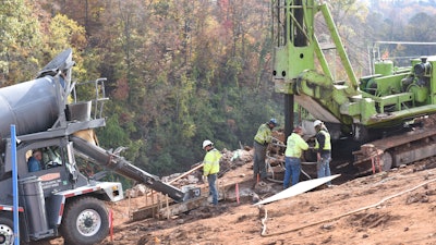 Workers pour concrete into a drilled hole.