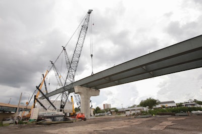 Workers pre-assemble two sections of girder on the ground before hoisting up to 200-ft.-long sections that weigh up to 200,000 lb.