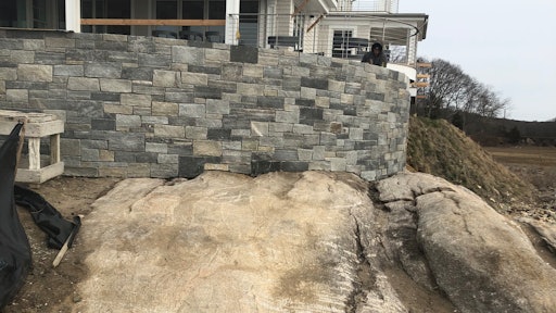 The finished patio landscape wall with stone veneer sits at the edge of the water, sharing a stone and traditional footing for bearing.