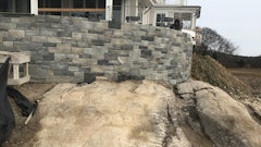 The finished patio landscape wall with stone veneer sits at the edge of the water, sharing a stone and traditional footing for bearing.
