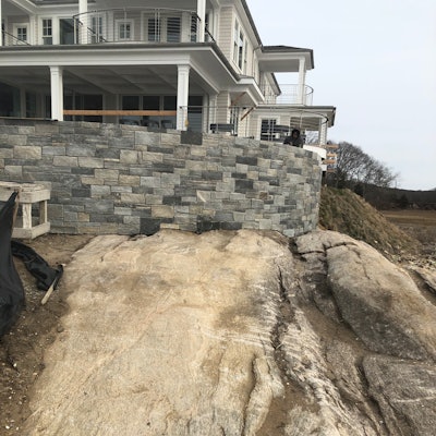 The finished patio landscape wall with stone veneer sits at the edge of the water, sharing a stone and traditional footing for bearing.