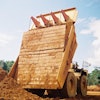 Carryback works against efficiency by reducing payload in the haul truck as residual material is left sticking to the sides and bottom of the truck, decreasing hauling capacity for subsequent loads.