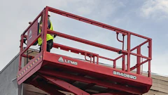 Red scissor lift raised next to warehouse building and shipping container