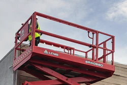 Red scissor lift raised next to warehouse building and shipping container