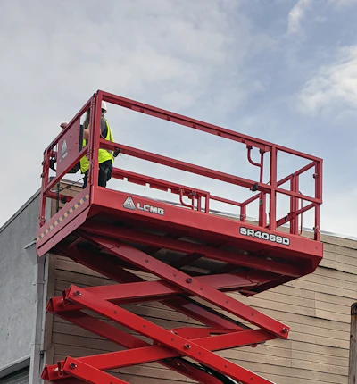 Red scissor lift raised next to warehouse building and shipping container