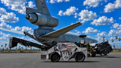 Decommissioned aircraft tail suspended above white ground support tug vehicle in desert aviation facility