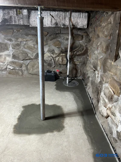 Adjustable steel support column set on a poured footing against a fieldstone wall.