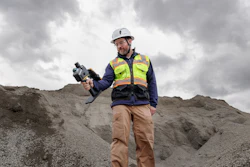 Construction worker in safety gear holding thermal imaging camera on gravel site