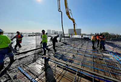 Construction workers pouring concrete on rooftop with city skyline and crane in background
