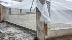 Greenhouse structure with white mesh netting and concrete foundation under construction