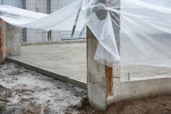 Greenhouse structure with white mesh netting and concrete foundation under construction