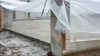 Greenhouse structure with white mesh netting and concrete foundation under construction