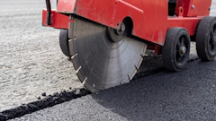 Red asphalt cutting machine with circular saw blade cutting through road pavement