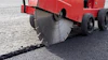 Red asphalt cutting machine with circular saw blade cutting through road pavement