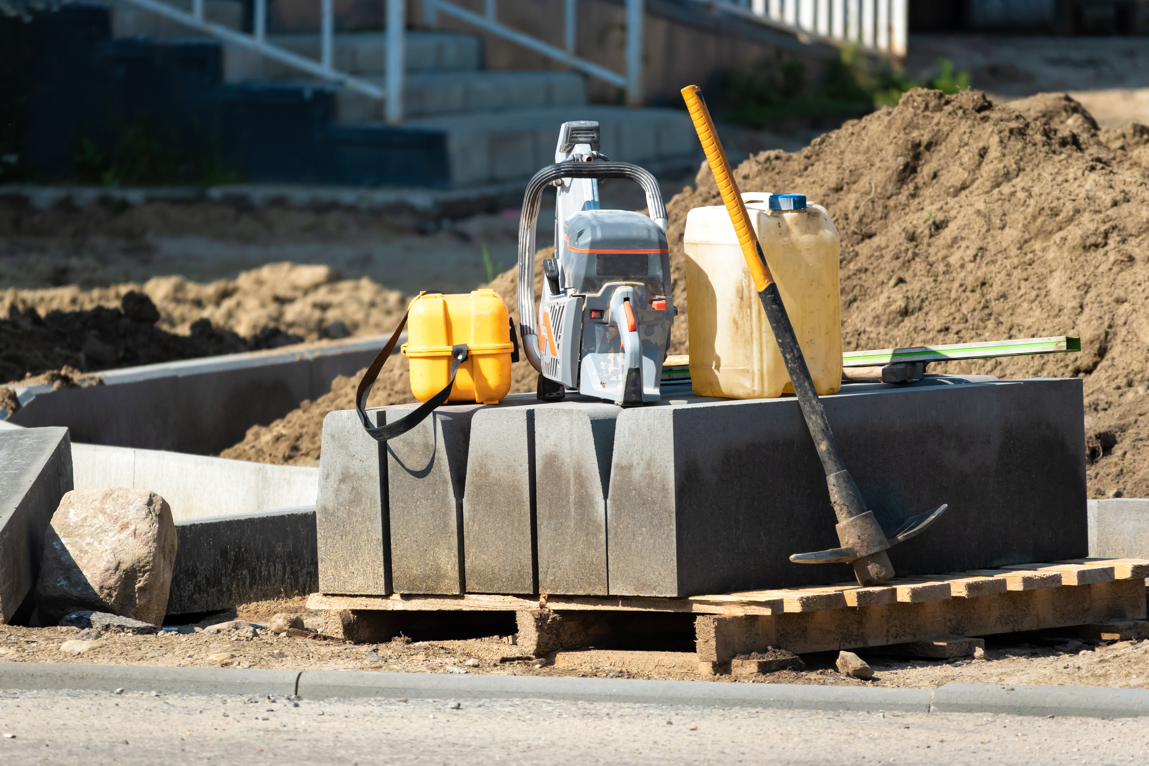 Construction site with compactor, safety vest, fuel container, and tools on concrete foundation