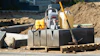 Construction site with compactor, safety vest, fuel container, and tools on concrete foundation