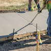 Construction workers finishing wet concrete with hand tools and measurement equipment on a residential driveway project.