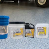 AmeriPolish concrete floor care products displayed in blue buckets and white containers on polished garage flooring