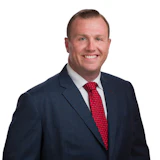 Professional headshot of a smiling man in navy blazer and red tie against white background