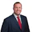 Professional headshot of a smiling man in navy blazer and red tie against white background Headshot