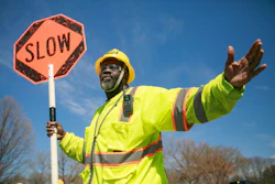 Construction worker in safety gear holding an orange SLOW traffic sign against blue sky
