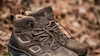 Three brown and black hiking boots with lace-up design and cushioned soles displayed in product view and outdoor terrain setting