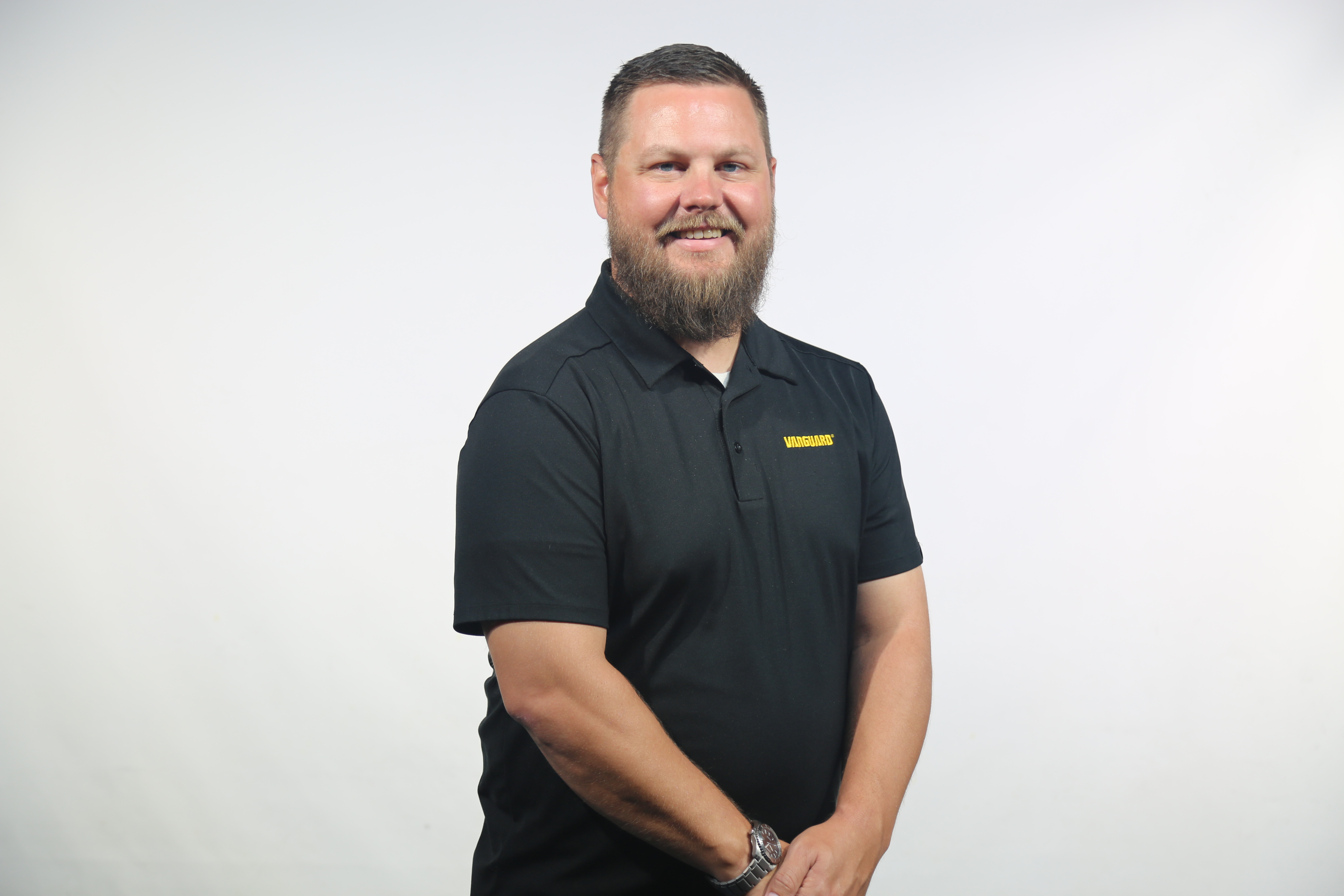 Professional man with beard wearing black DeWALT polo shirt, smiling at camera against white background