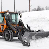 Orange wheel loader with Hilltip snow plow clearing snow from a winter landscape