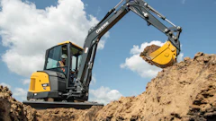 Yellow and black John Deere mini excavator with extended boom digging in sandy soil under blue sky
