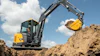 Yellow and black John Deere mini excavator with extended boom digging in sandy soil under blue sky