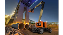 Orange JLG telescopic boom lift operating at dusk near large industrial pipes and concrete structure
