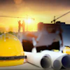 Yellow safety helmet with construction blueprints, ear protection, and workers on building site at sunset