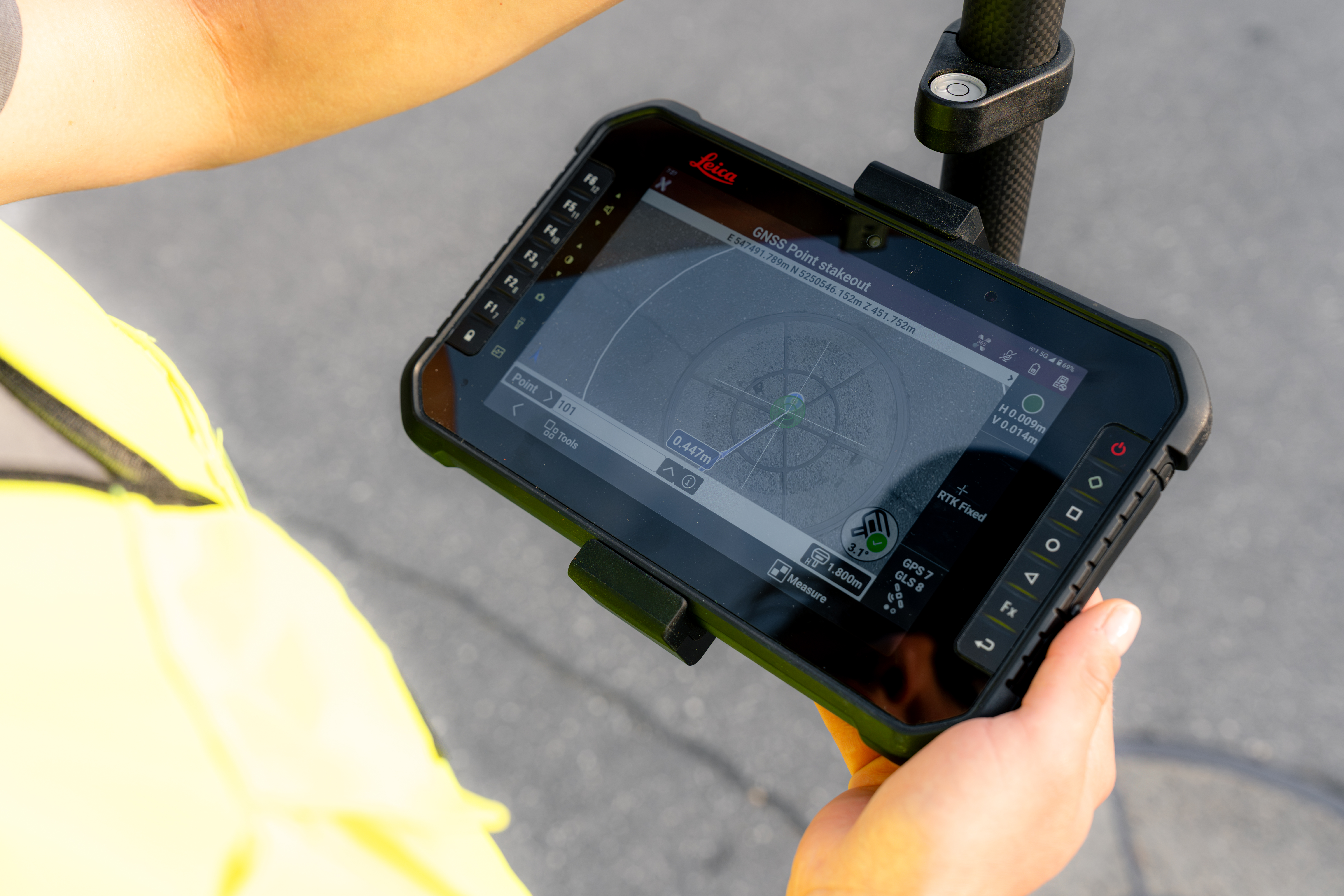 Worker in yellow safety vest holding rugged tablet displaying surveying or mapping software outdoors